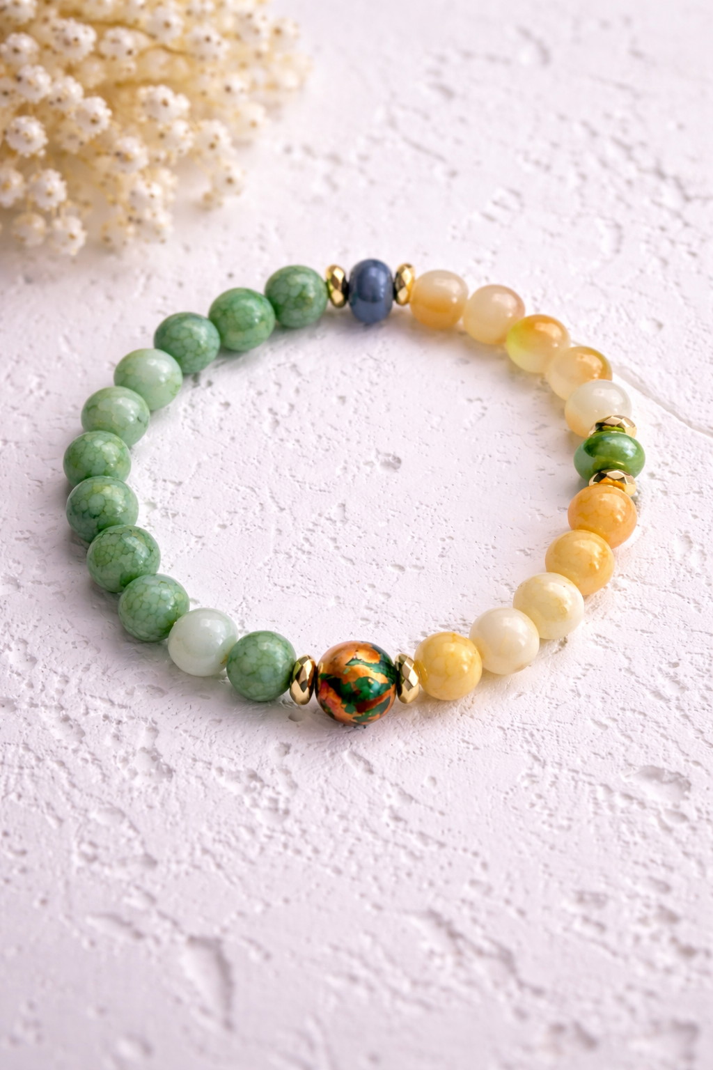 Handgemachtes grünes Perlenarmband mit gelblichen Glasperlen und goldenen Akzenten auf hellem Hintergrund